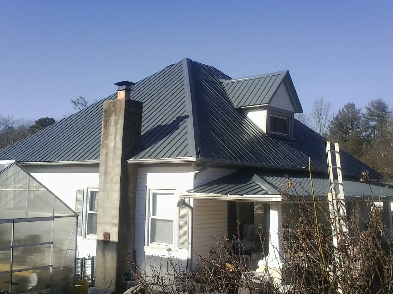 Dark blue standing seam metal roof on a white farmhouse with dormer in Marion